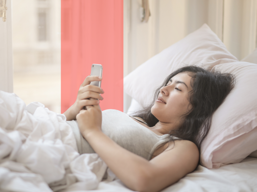 Kvinde læser på mobil i sengen og smiler